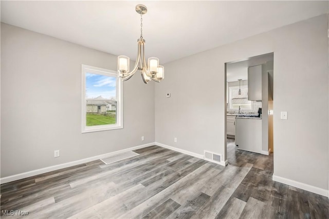 unfurnished dining area featuring visible vents, wood finished floors, a chandelier, and baseboards