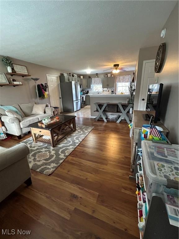 living room with a textured ceiling, wood finished floors, and a ceiling fan