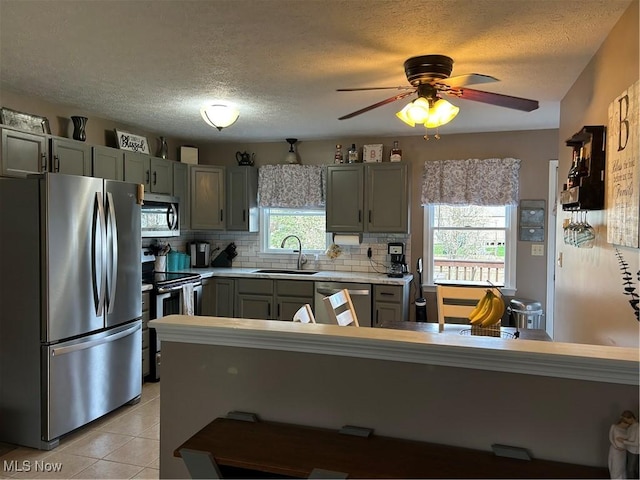 kitchen with a sink, decorative backsplash, light tile patterned floors, light countertops, and appliances with stainless steel finishes