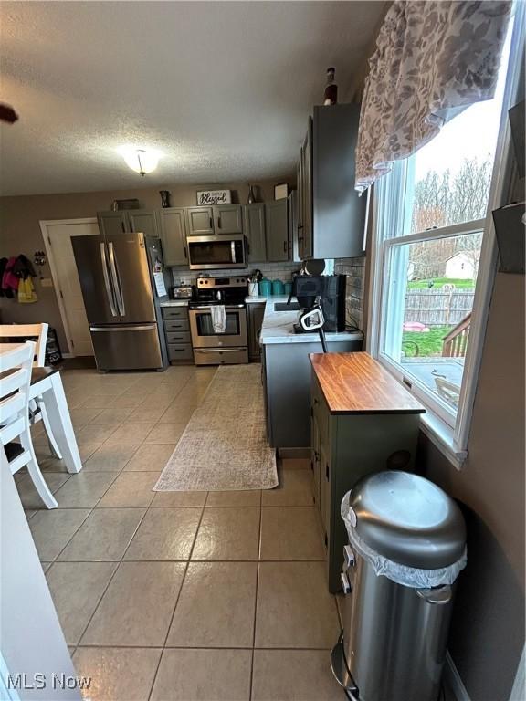 kitchen with light tile patterned flooring, gray cabinets, stainless steel appliances, and decorative backsplash