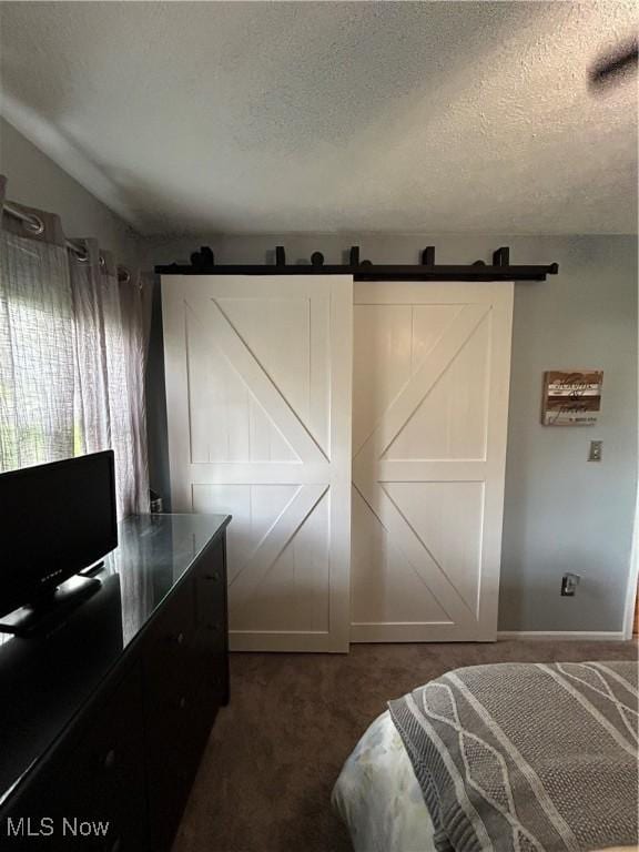 bedroom with a barn door, a textured ceiling, dark colored carpet, and baseboards