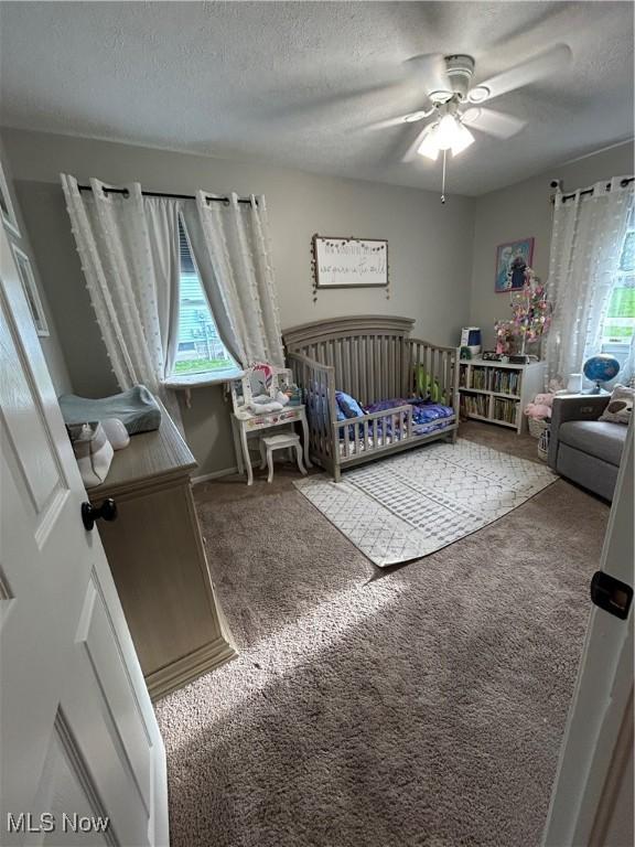 carpeted bedroom with a crib, ceiling fan, and a textured ceiling