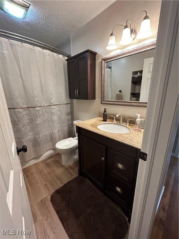 full bath featuring wood finished floors, toilet, vanity, curtained shower, and a textured ceiling