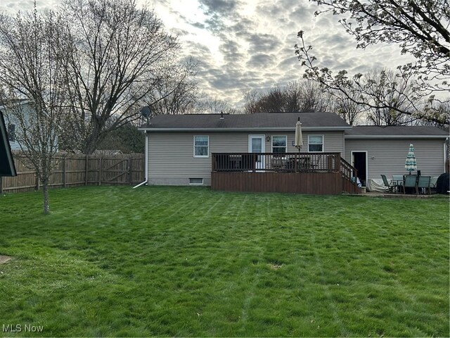 rear view of house with a lawn, a deck, and fence