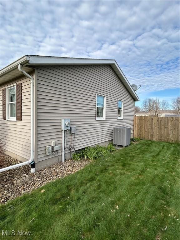 view of side of property with a lawn, central air condition unit, and fence