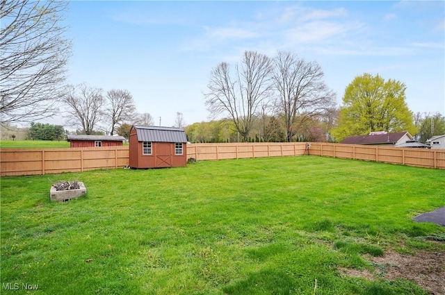 view of yard featuring a storage unit, an outbuilding, a fenced backyard, and a fire pit
