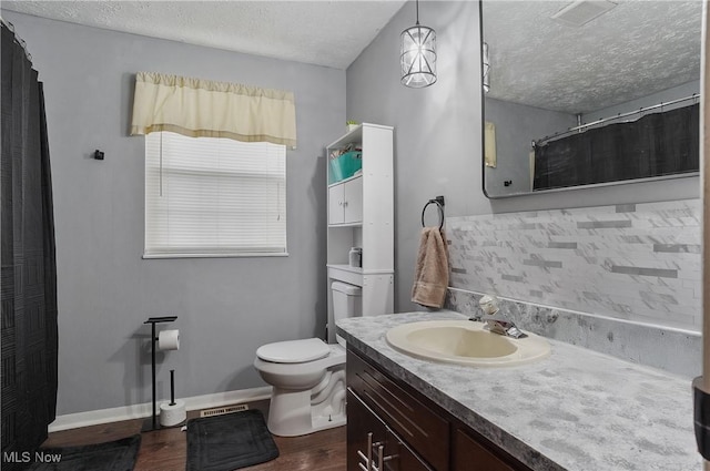 full bath featuring a textured ceiling, baseboards, toilet, wood finished floors, and vanity