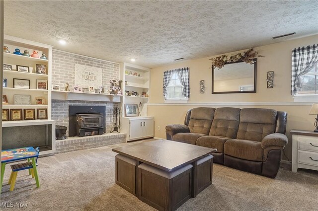 carpeted living room with a textured ceiling, visible vents, and a wood stove