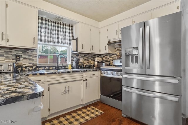 kitchen with tasteful backsplash, a sink, appliances with stainless steel finishes, dark countertops, and dark wood finished floors