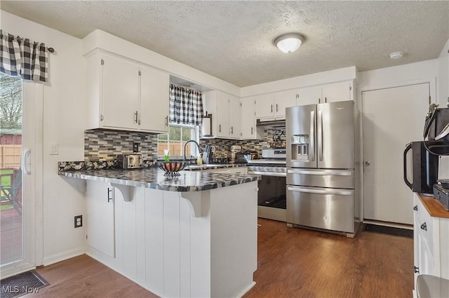 kitchen with a textured ceiling, tasteful backsplash, stainless steel appliances, dark wood-type flooring, and a peninsula
