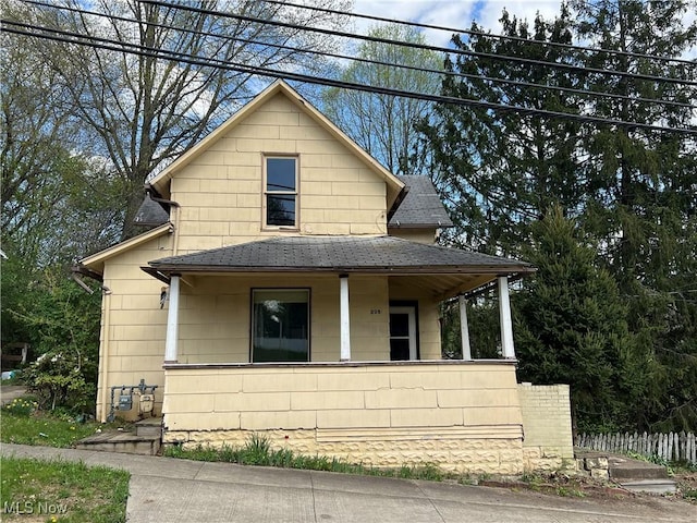 view of front facade featuring fence, a shingled roof, and a porch