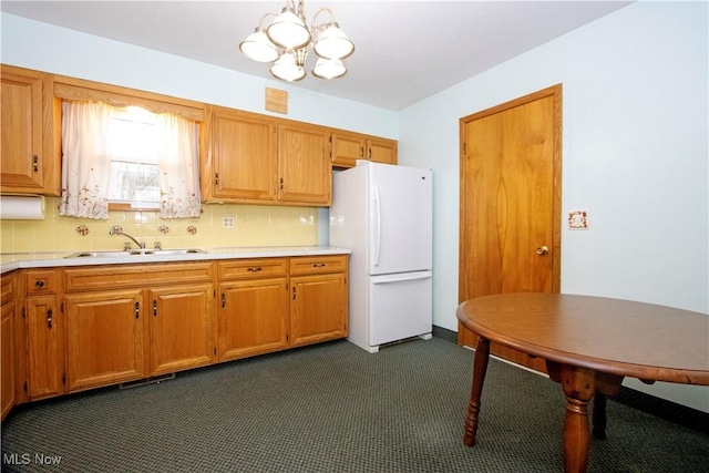 kitchen featuring freestanding refrigerator, light countertops, dark colored carpet, a sink, and a notable chandelier