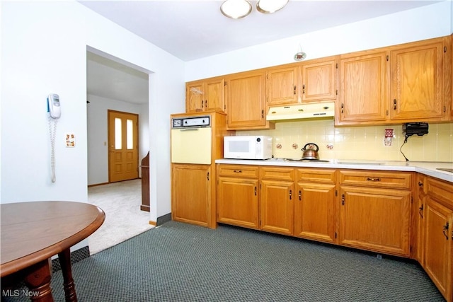 kitchen with under cabinet range hood, white appliances, dark carpet, backsplash, and light countertops