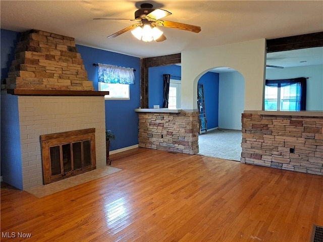 49197 John Tomcho Rd, Cumberland, OH 43732 - unfurnished living room featuring a ceiling fan, wood finished floors, a large fireplace, arched walkways, and baseboards