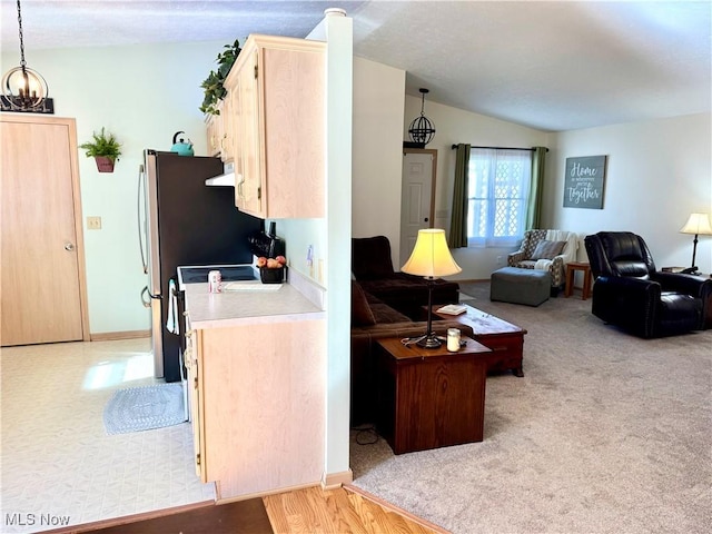 living area featuring light colored carpet, a notable chandelier, vaulted ceiling, and baseboards