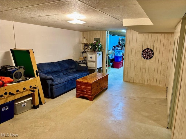 living room featuring wooden walls, a drop ceiling, concrete block wall, and finished concrete floors