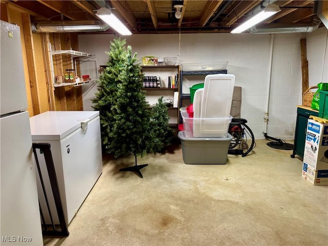 unfinished basement featuring fridge, freestanding refrigerator, and concrete block wall