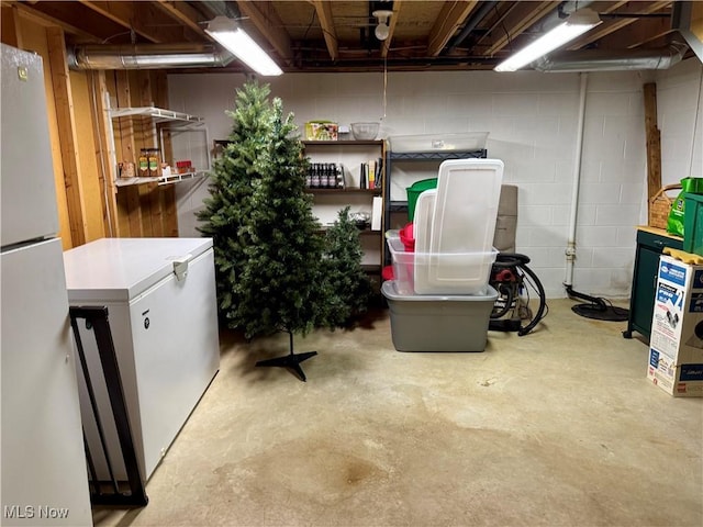 unfinished below grade area featuring concrete block wall, refrigerator, and freestanding refrigerator