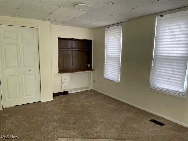 unfurnished bedroom with a paneled ceiling, visible vents, baseboards, and carpet floors