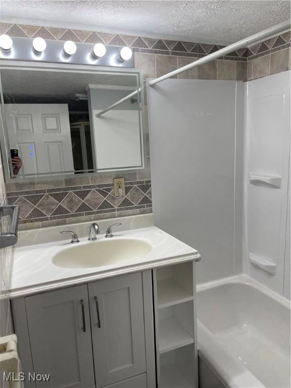 bathroom with a textured ceiling, bathing tub / shower combination, vanity, and decorative backsplash