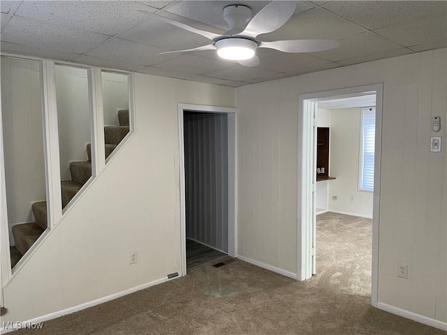 carpeted empty room with a ceiling fan, stairway, a drop ceiling, and baseboards