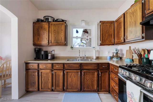 kitchen featuring a sink, under cabinet range hood, stainless steel range with gas cooktop, light countertops, and arched walkways
