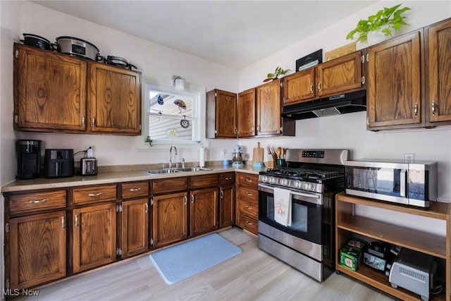 kitchen with light wood-style flooring, stainless steel appliances, under cabinet range hood, light countertops, and a sink