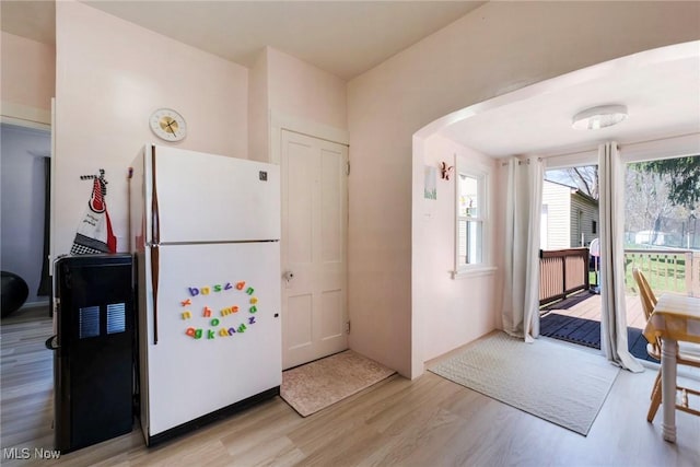 kitchen with light wood-style flooring, freestanding refrigerator, and arched walkways