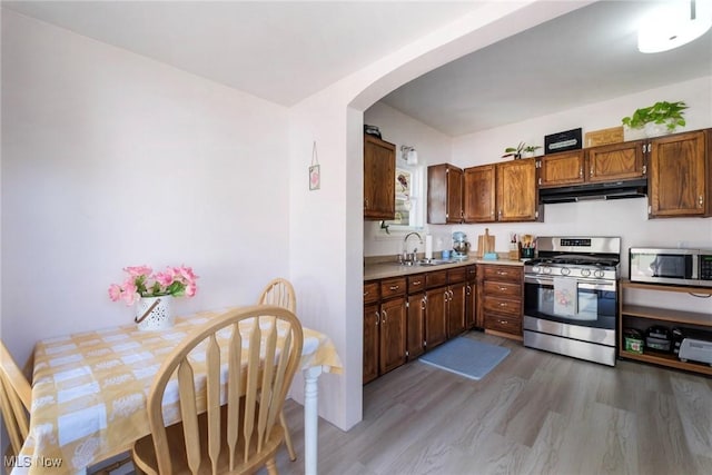kitchen with a sink, stainless steel appliances, under cabinet range hood, arched walkways, and wood finished floors