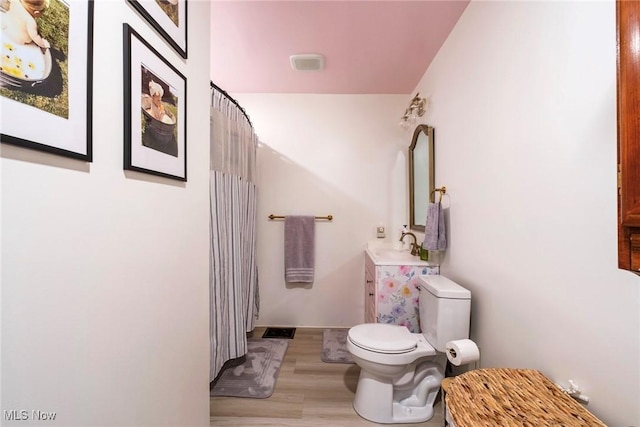 bathroom with wood finished floors, a shower with curtain, toilet, vanity, and visible vents