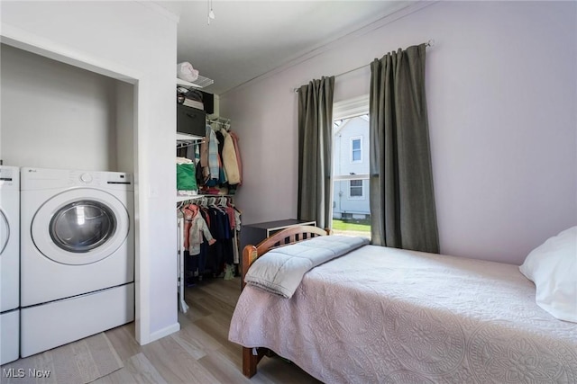 bedroom featuring light wood-style flooring, washing machine and dryer, ornamental molding, cooling unit, and a walk in closet