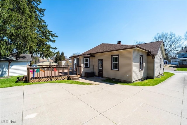 bungalow with roof with shingles, a wooden deck, and a patio area