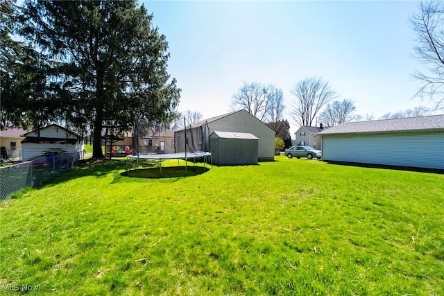 view of yard featuring a trampoline, fence, a storage unit, and an outbuilding