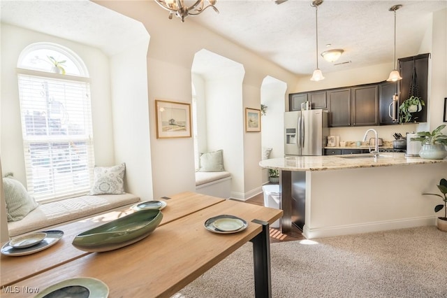 kitchen featuring light stone countertops, arched walkways, decorative light fixtures, stainless steel fridge, and a sink