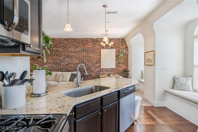 kitchen with a sink, visible vents, stainless steel appliances, dark brown cabinetry, and brick wall