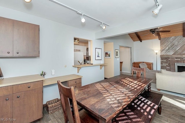 dining room featuring a fireplace, vaulted ceiling, rail lighting, wood finished floors, and a ceiling fan