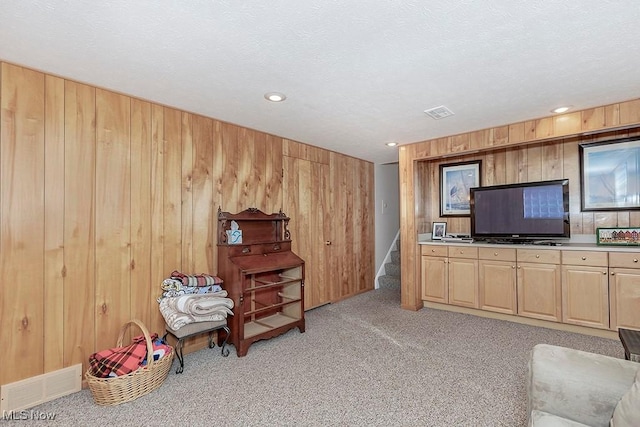 living area featuring stairs, visible vents, wood walls, and light colored carpet