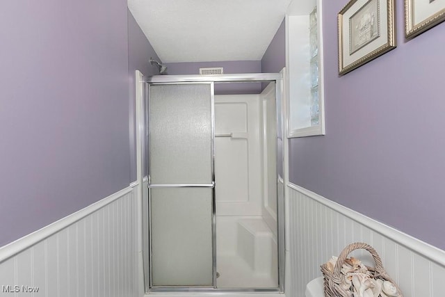 full bath with a decorative wall, a shower stall, and wainscoting