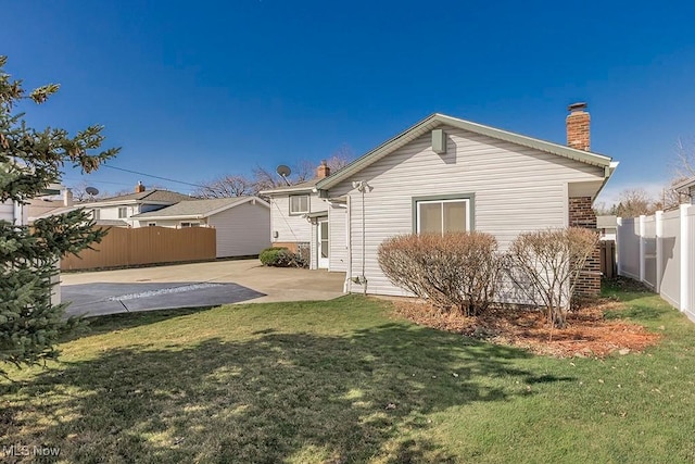 back of house featuring a chimney, fence, a patio, and a lawn