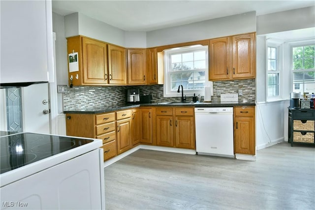 kitchen with a sink, dark countertops, light wood finished floors, white appliances, and brown cabinetry