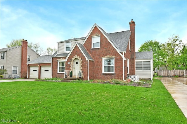 tudor house with driveway, roof with shingles, a front yard, and brick siding