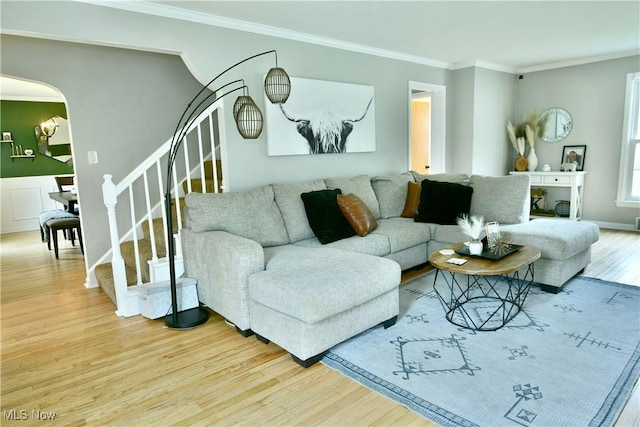 living room featuring stairway, wood finished floors, crown molding, and arched walkways