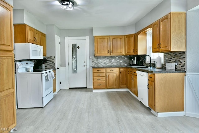 kitchen with a sink, backsplash, light wood-style flooring, white appliances, and dark countertops