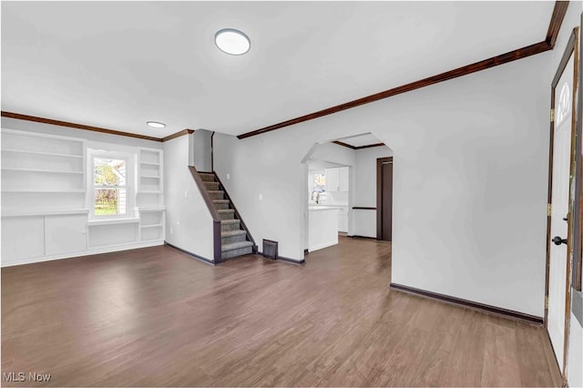 135 W Bagley Rd, Berea, OH 44017 - unfurnished living room with dark wood finished floors, arched walkways, built in shelves, stairway, and crown molding