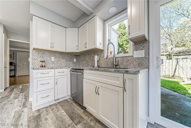 kitchen featuring light stone countertops, tasteful backsplash, white cabinets, dishwasher, and a sink