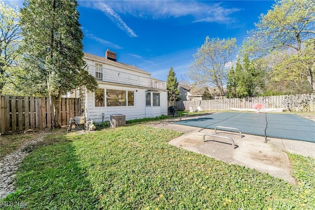 back of house featuring cooling unit, a fenced in pool, a chimney, a lawn, and a fenced backyard