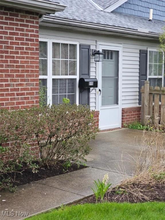 property entrance with fence, a shingled roof, and brick siding