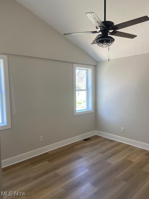 spare room with baseboards, ceiling fan, dark wood-type flooring, and vaulted ceiling