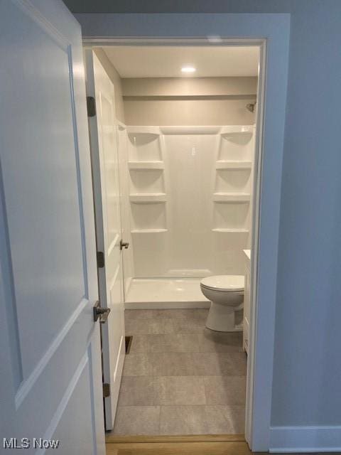 bathroom featuring toilet, tile patterned flooring, and a stall shower