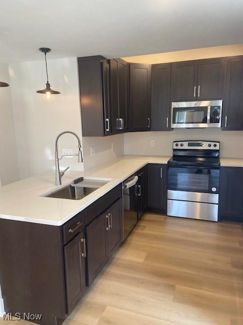 kitchen with a sink, appliances with stainless steel finishes, light countertops, light wood-type flooring, and a peninsula